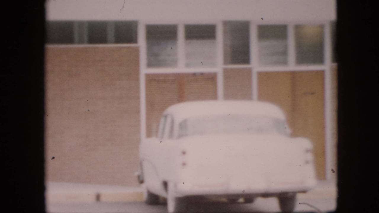 White car parked outside a brick building with glass-panel doors and windows.