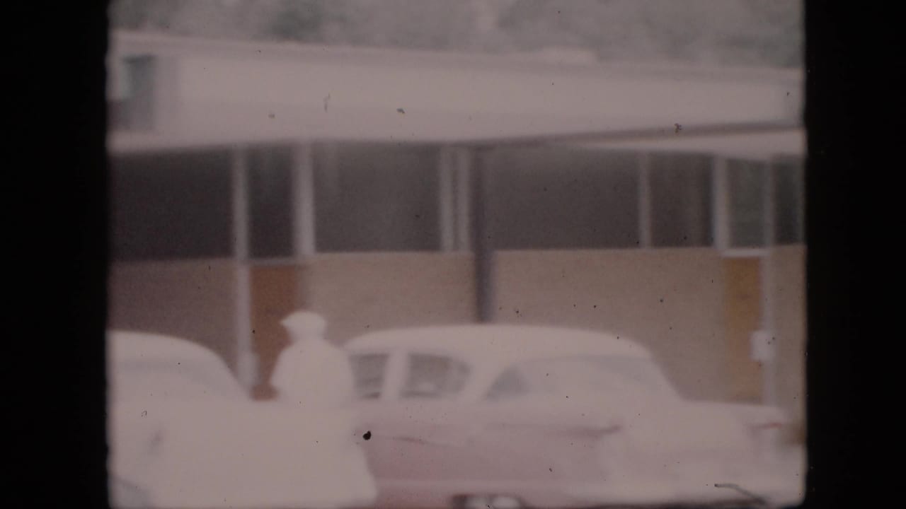 Bundled pedestrians move near snow-covered cars outside a roadside commercial building in Pennsylvania, 1958 home-movie footage.