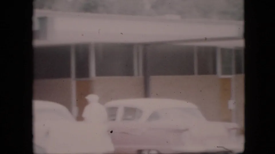 Bundled pedestrians move near snow-covered cars outside a roadside commercial building in Pennsylvania, 1958 home-movie footage.