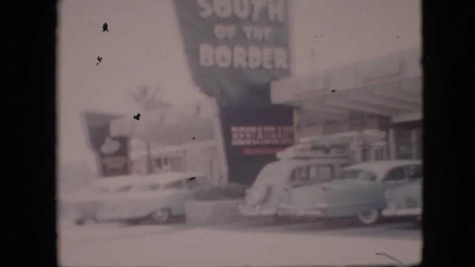 A large South of the Border sign rises above classic cars in a snowy roadside parking lot in Pennsylvania footage identified as 1958.
