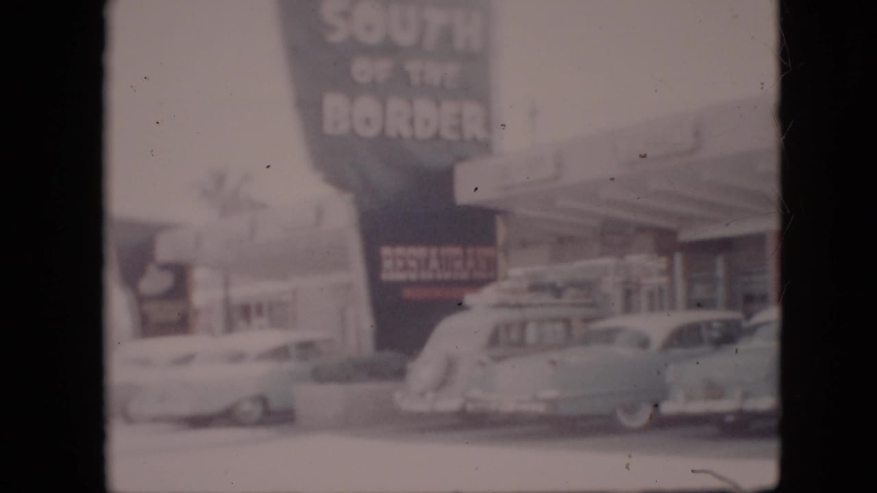 Roadside South of the Border sign above parked 1950s cars and a service building.