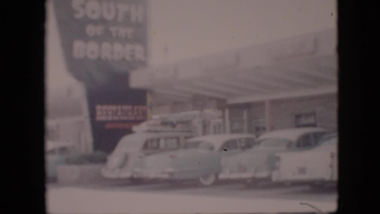 Soft 8mm view of a 1958 Pennsylvania roadside restaurant or gas station with a large South of the Border sign and several parked cars.