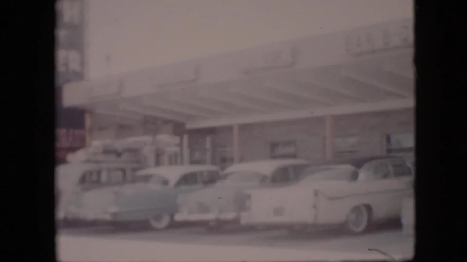 1958 Pennsylvania home-movie frame showing mid-century cars lined up near a covered roadside restaurant or service-station area.