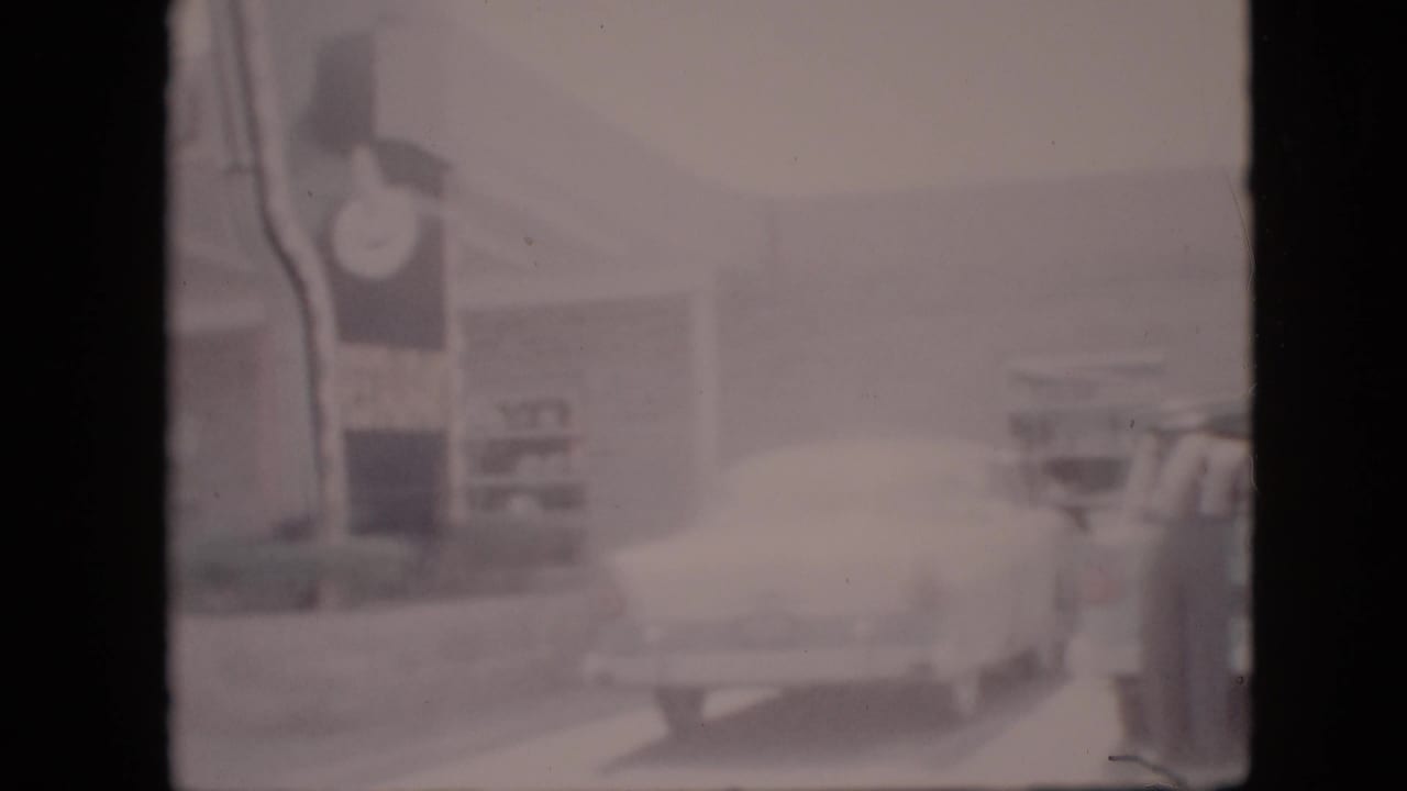Rear of a light-colored car near the BAR-B-Q restaurant and street edge.