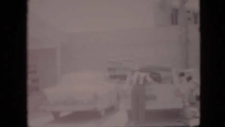 1958 Pennsylvania 8mm frame showing a station wagon or light-colored car near the roadside BAR-B-Q restaurant, with the clock sign and restaurant frontage softened by exposure haze.