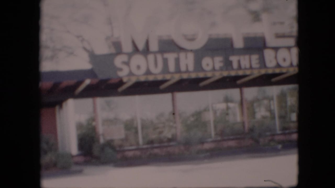 1958 8mm home-movie frame showing the South of the Border Motel sign above windows, shrubs, and a covered entry, with no people visible.