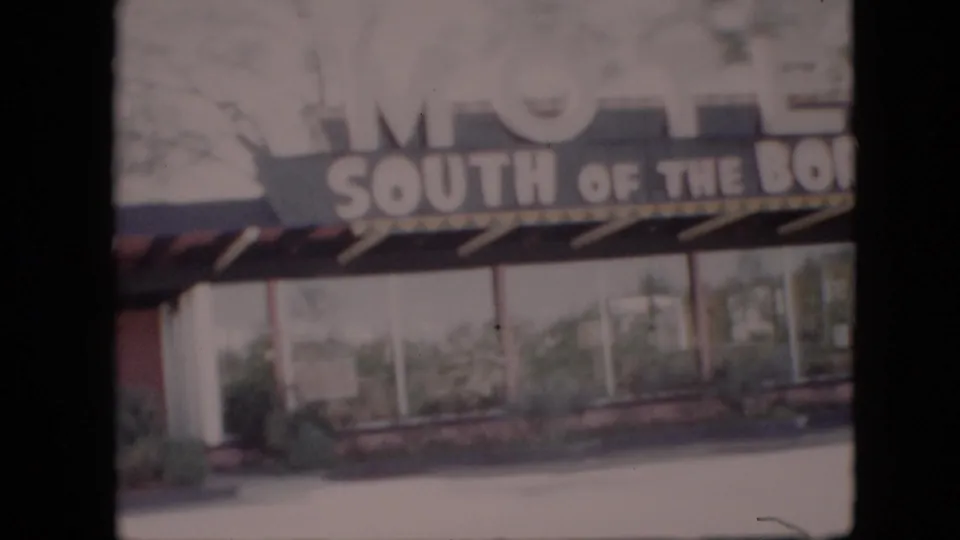 1958 8mm home-movie frame showing the South of the Border Motel sign above windows, shrubs, and a covered entry, with no people visible.