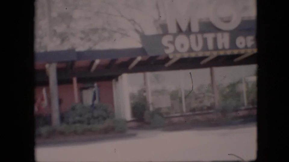 1958 8mm frame of the South of the Border Motel exterior, with bold sign letters, a canopy, columns, windows, and landscaping visible.