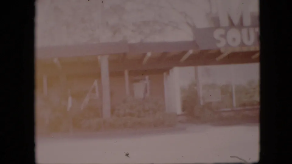 Overexposed 1958 8mm frame showing part of the South of the Border Motel sign above a covered entrance with white columns and glass frontage.