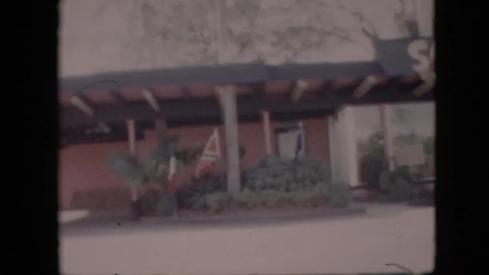 1958 Pennsylvania 8mm frame showing a mid-century building exterior with a covered entrance, support columns, shrubbery, and a small flag near the facade.