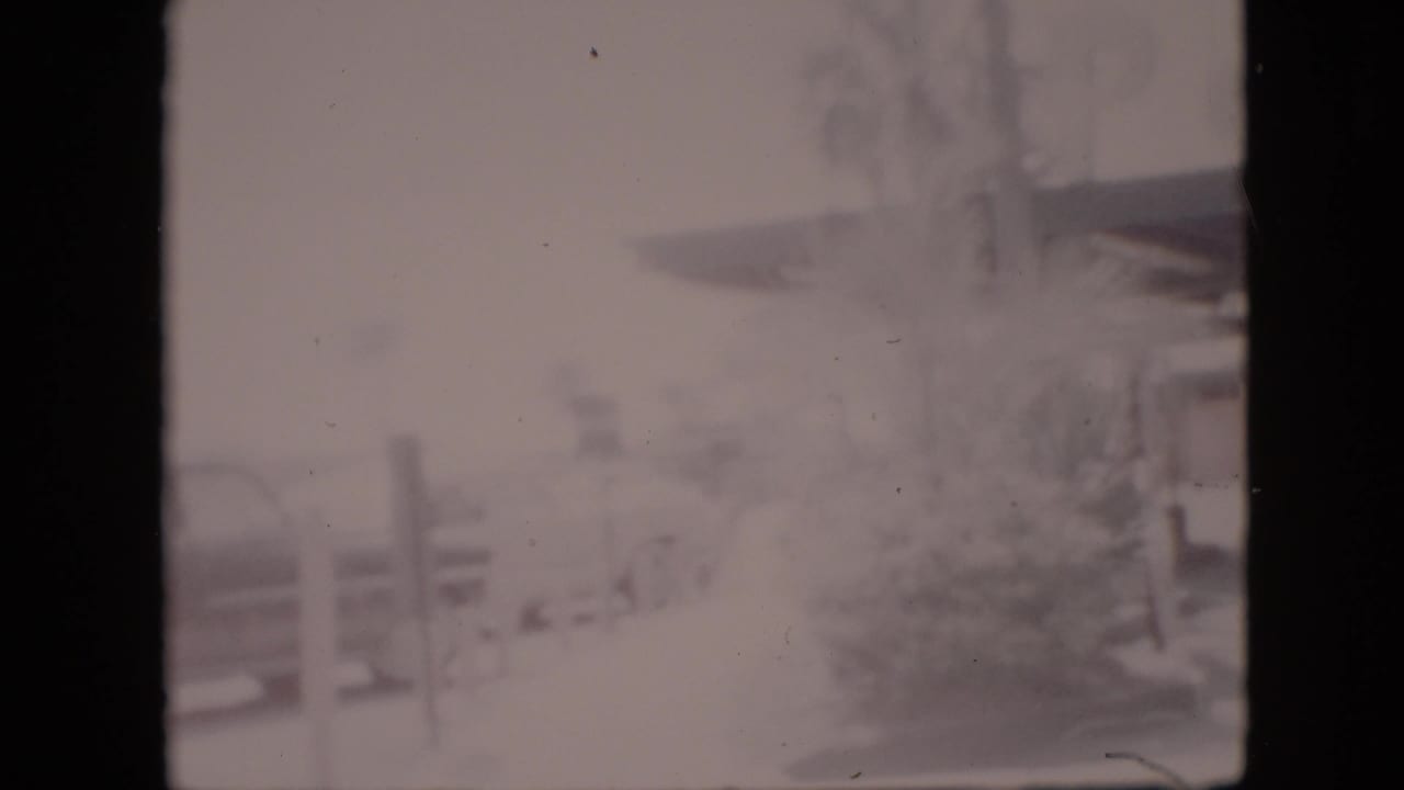 Soft, washed-out 1958 Pennsylvania home-movie frame showing a roadside building canopy, vertical posts, faint landscaping, and indistinct signage that may identify the business.