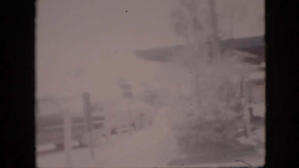 Soft, washed-out 1958 Pennsylvania home-movie frame showing a roadside building canopy, vertical posts, faint landscaping, and indistinct signage that may identify the business.