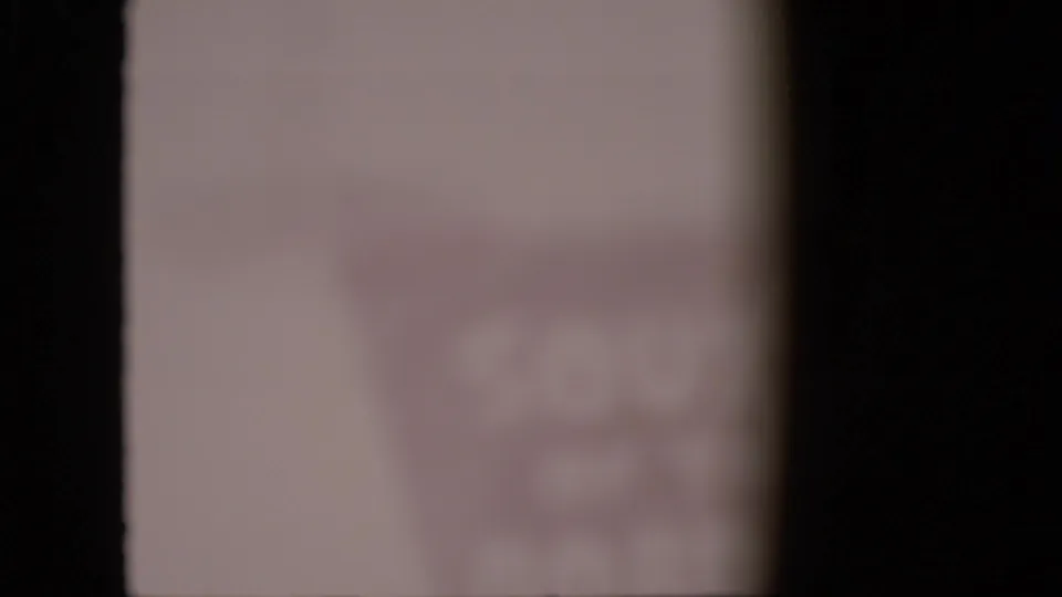 Extremely soft 1958 Pennsylvania home-movie frame showing a blurred sign or facade detail, with the business identity unreadable because of focus loss and fading.