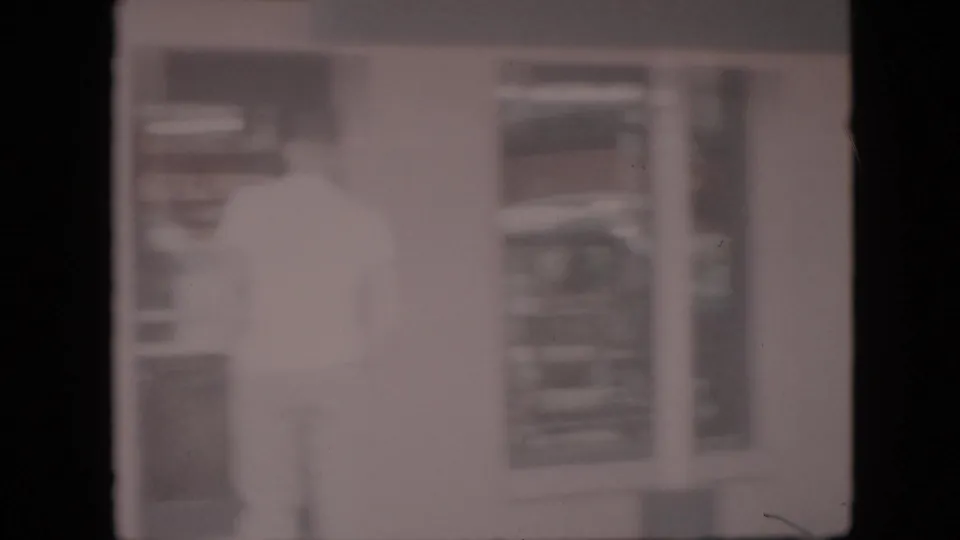 In this 1958 Pennsylvania 8mm home-movie frame, a light-clothed man appears near a doorway or interior opening, seen through heavy blur and overexposure.