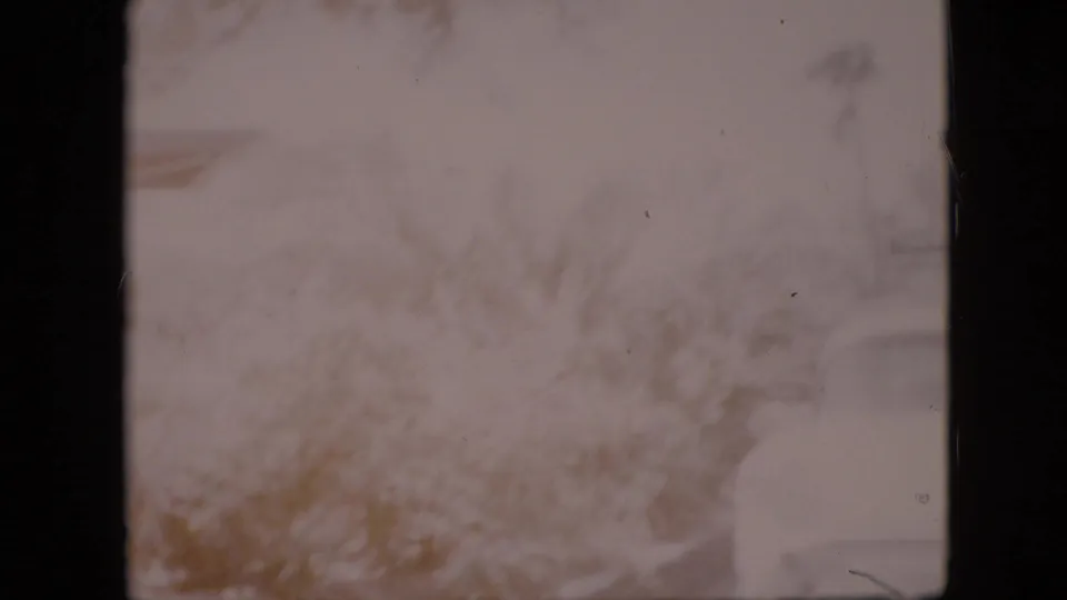 The frame shows a washed-out section of the home-movie scene with pale ground, blurred vegetation, and faint structural shapes from the same 1958 Pennsylvania clip.