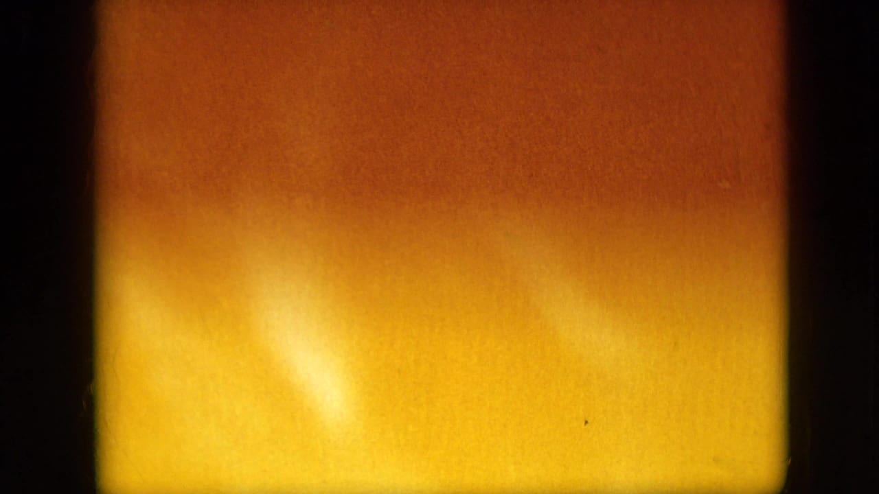 A 1958 Pennsylvania 8mm frame showing an abstract warm orange and yellow exposure field with dark vertical film borders and visible grain.