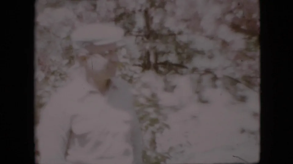 In 1958 Pennsylvania home-movie footage, a middle-aged man in a light shirt and cap appears partly hidden among pale flowering branches.
