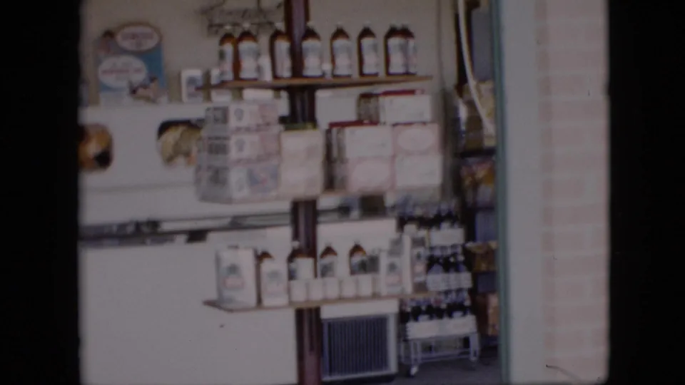 The final frame shows the store's stocked shelves and bottled goods near a white refrigerated case, recorded with soft 8mm home-movie focus.