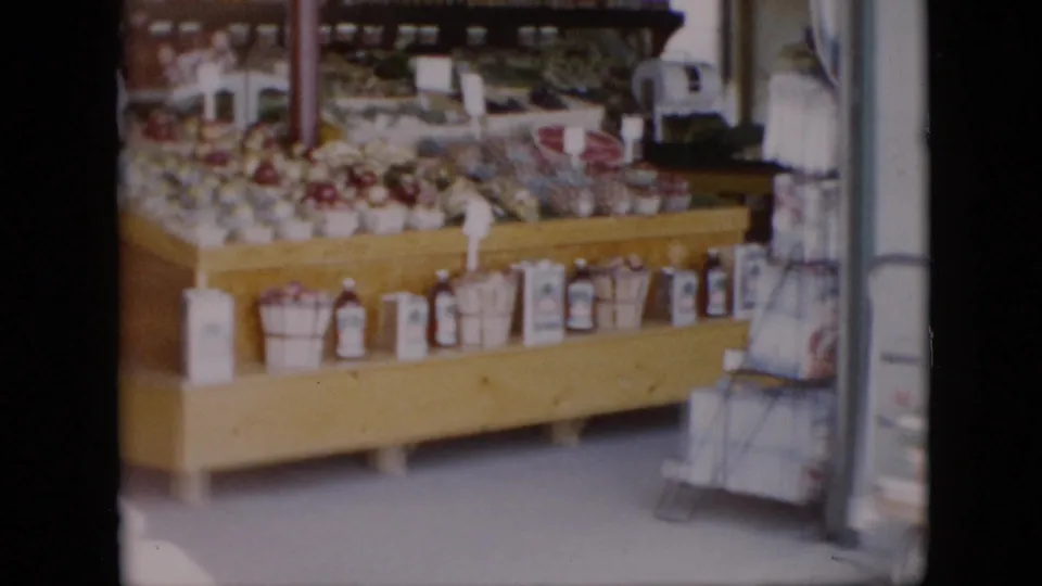 1958 Pennsylvania grocery interior showing a wooden produce table packed with fruit baskets, bottles and cans along the lower shelf, and side shelving near the aisle.