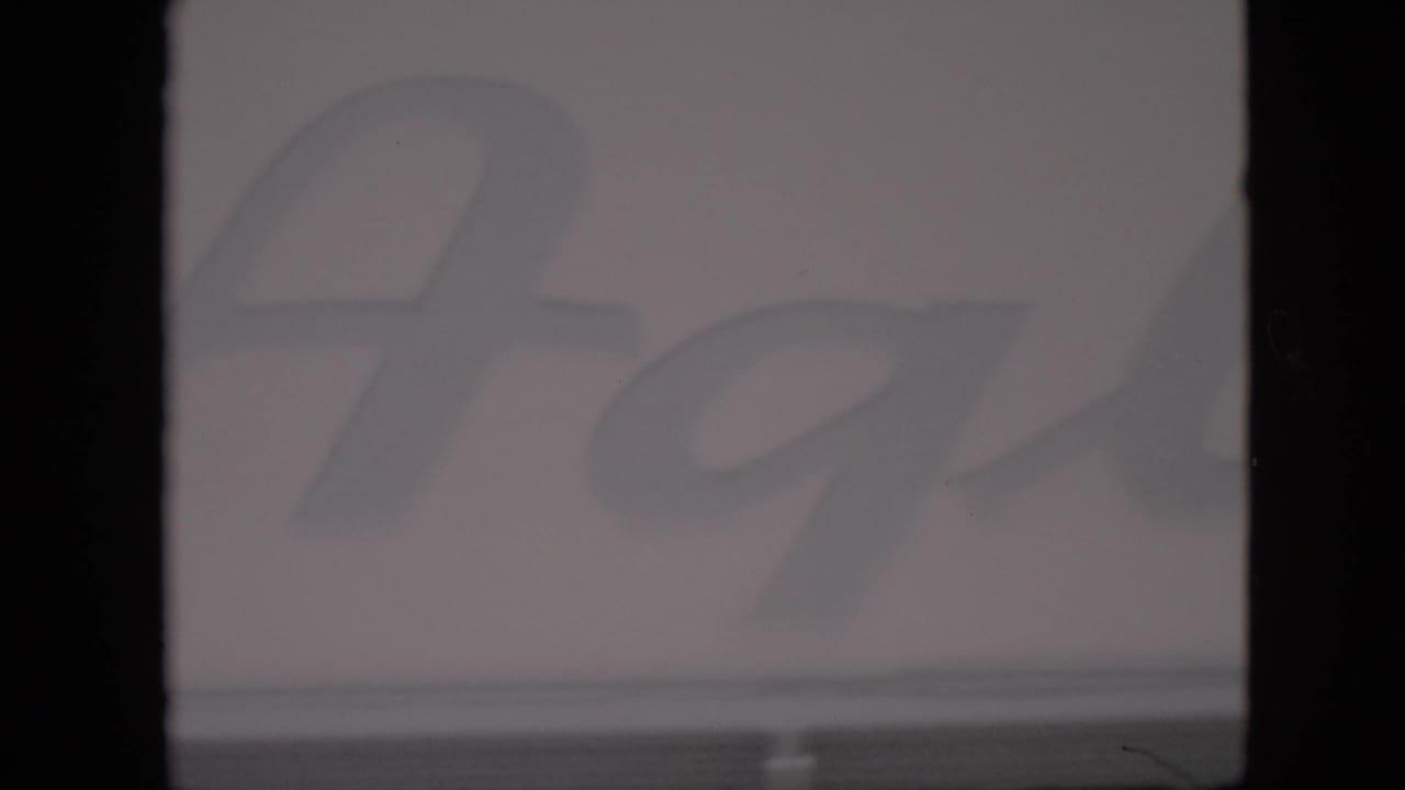 1958 Pennsylvania 8mm frame showing part of a faded cursive farm-stand sign, soft focus, muted exposure, and visible film-gate edges.