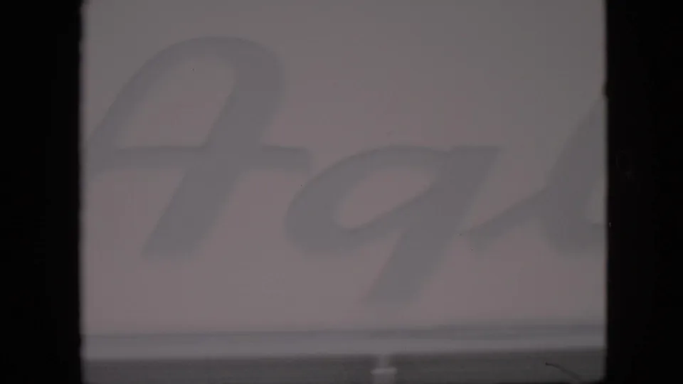 1958 Pennsylvania 8mm frame showing part of a faded cursive farm-stand sign, soft focus, muted exposure, and visible film-gate edges.