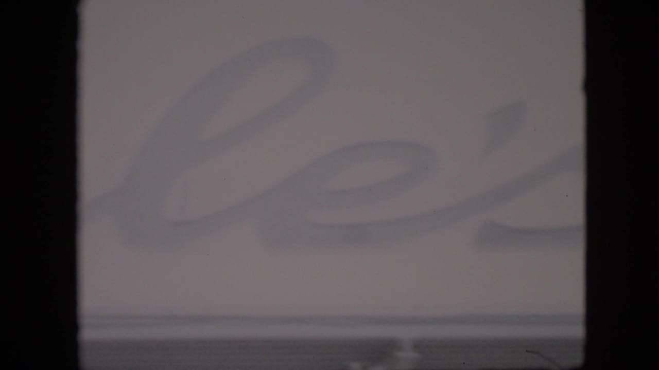 Soft 1958 Pennsylvania home-movie frame with faded cursive lettering across a pale farm-stand sign and strong dark frame borders.