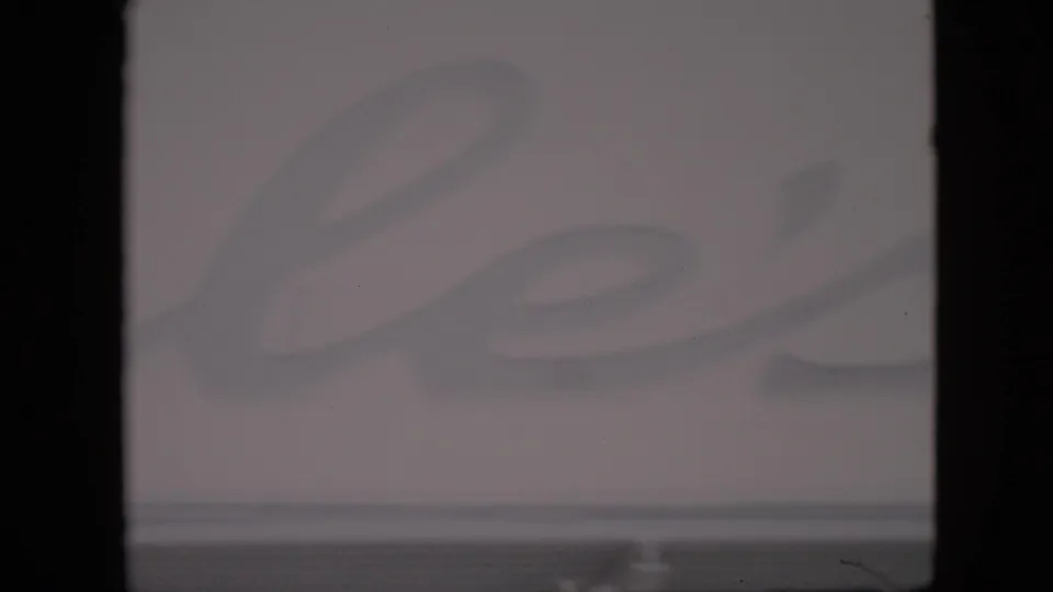 Soft 1958 Pennsylvania home-movie frame with faded cursive lettering across a pale farm-stand sign and strong dark frame borders.