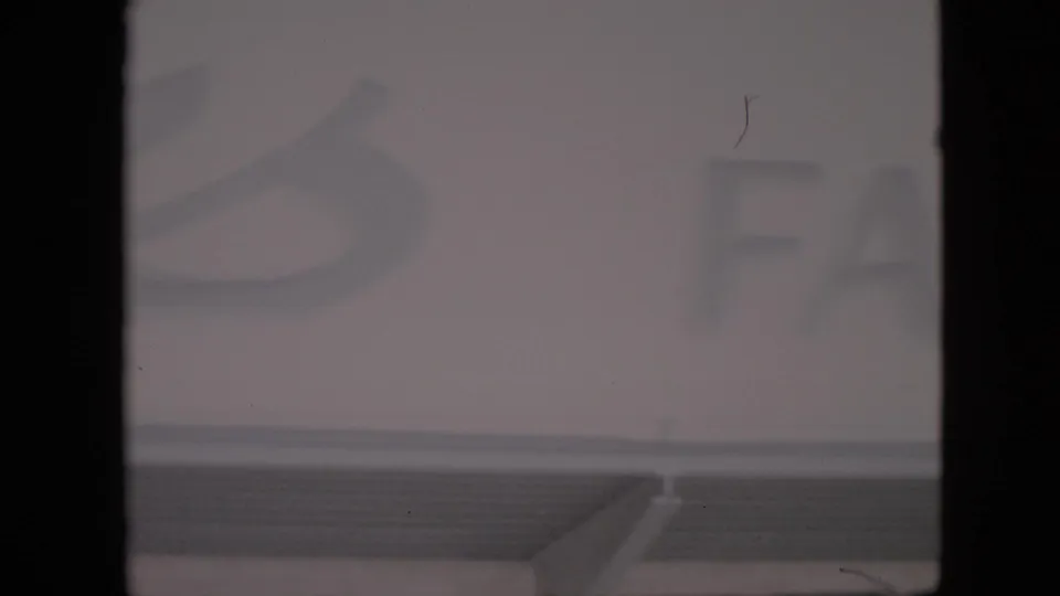 1958 Pennsylvania 8mm frame showing a cropped farm-stand sign, faint lettering, a dark film border, and visible surface scratches.