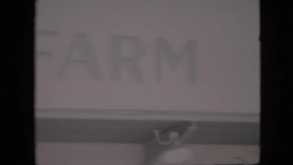 1958 Pennsylvania home-movie frame showing partial block lettering on a farm-stand sign, with a small support bracket visible below the sign edge.