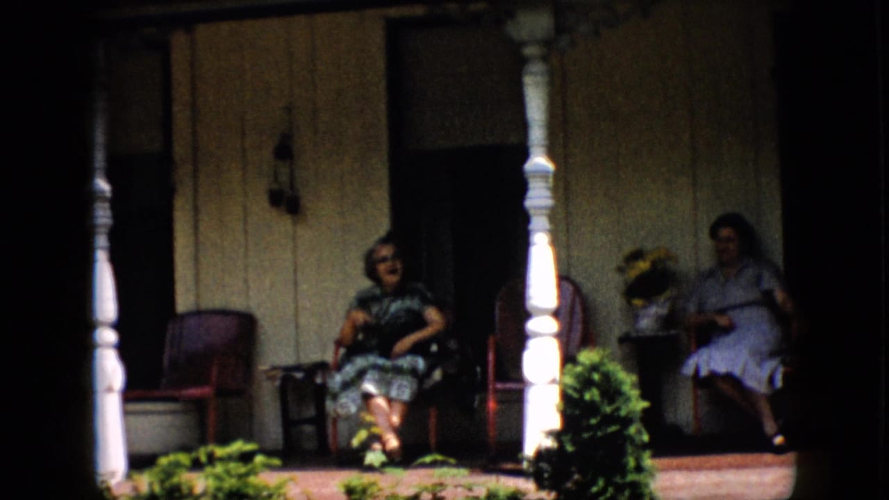 A woman in a dark dress sits near a porch column while another woman sits farther back in shadow.