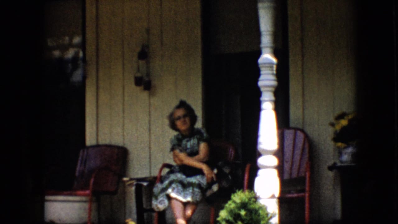 Woman smiling from a red chair on a shaded porch.