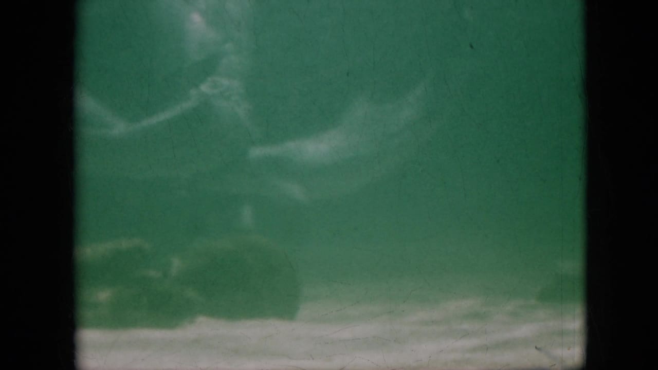 1958 Pennsylvania 8mm frame showing a dolphin-like form gliding through green aquarium water with pale tank bands and visible film wear.