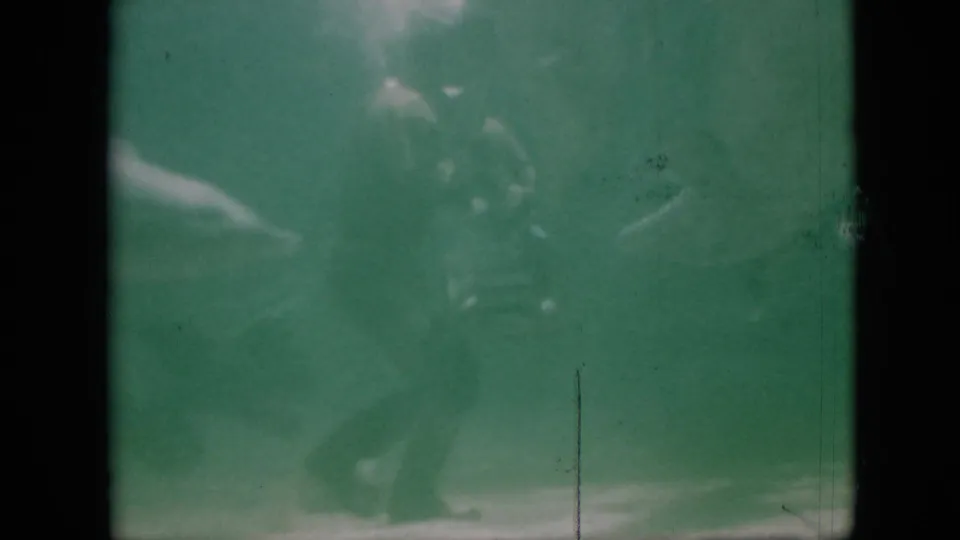 1958 Pennsylvania 8mm frame with faint dolphin movement in green aquarium water, softened by exposure, scratches, and film aging.