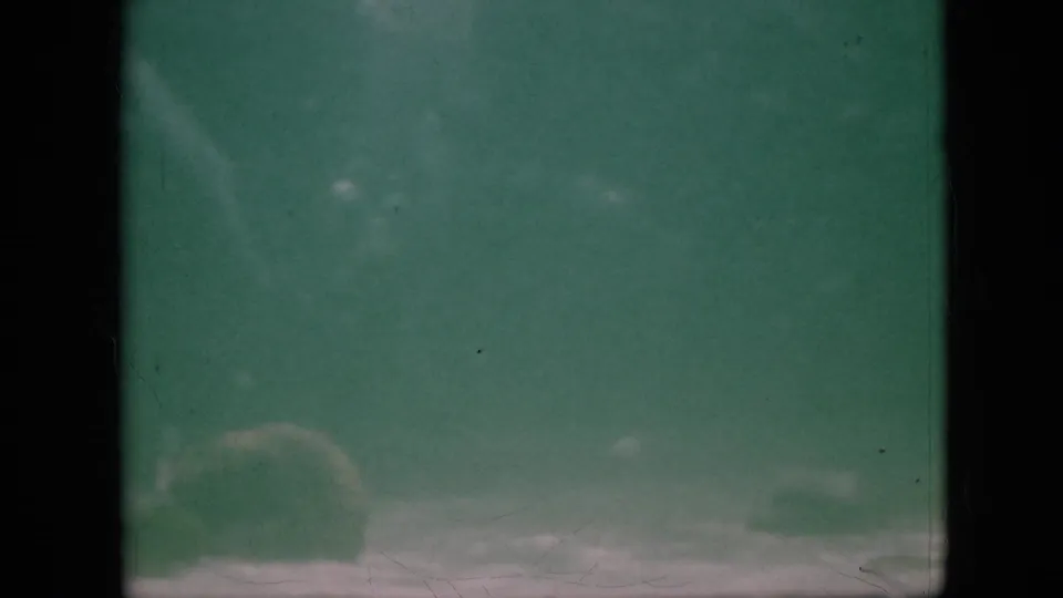 1958 Pennsylvania 8mm frame showing low-visibility green water with faint fish shapes near the lower edge, a dark central band, grain, and scratches.