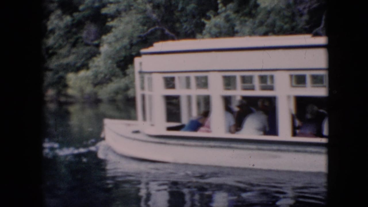 A white enclosed tour boat passes along a calm tree-lined river in Pennsylvania, with seated passengers visible through the cabin windows in 1958 home-movie footage.