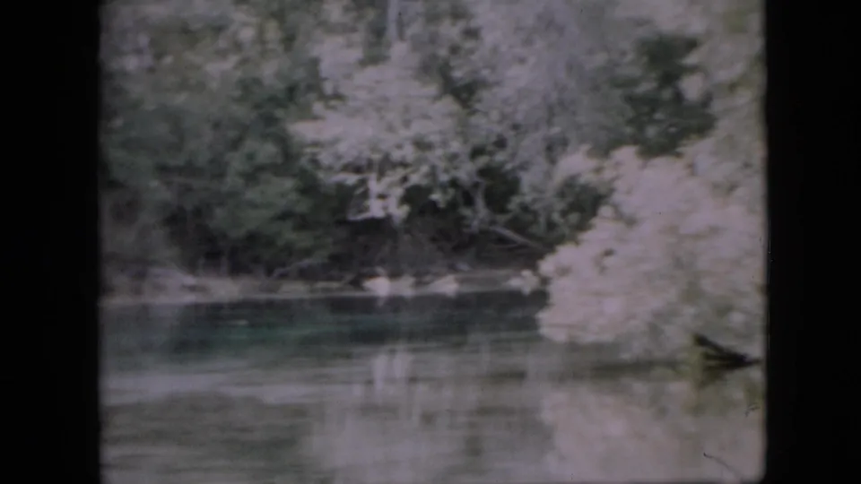 1958 Pennsylvania home-movie frame showing a quiet river bend bordered by trees and pale shoreline, with muted reflections across the water.
