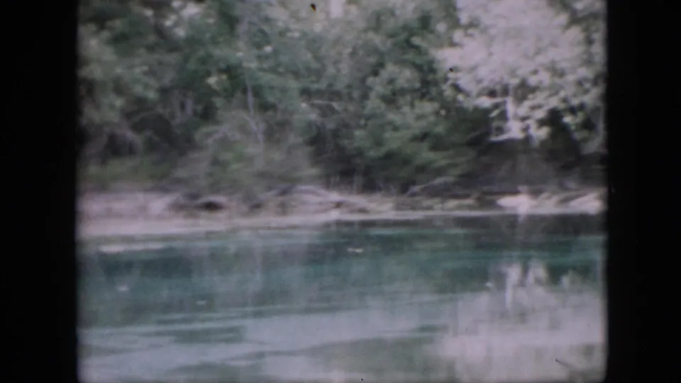 Soft 8mm view from a Pennsylvania waterway in 1958, with a wooded bank and blurred reflections on the calm river surface.