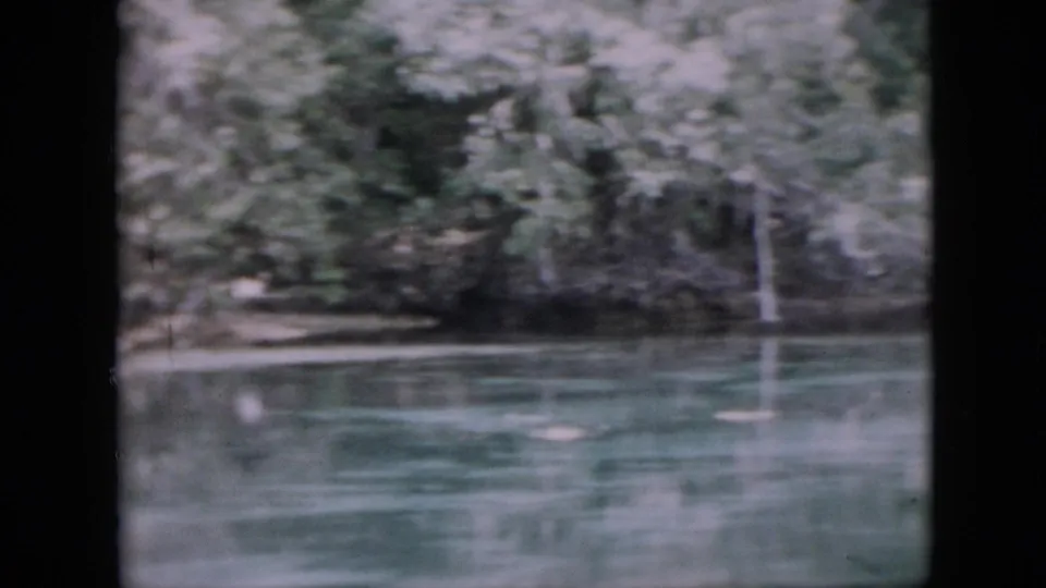 1958 Pennsylvania frame of greenish river water with blurred tree reflections and a shaded wooded shoreline in the background.