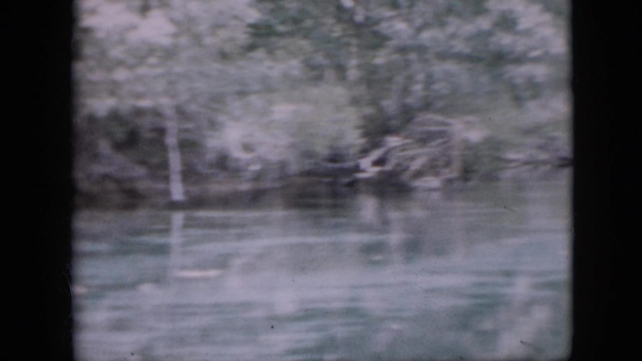 1958 Pennsylvania 8mm frame showing calm river water with soft reflections of dense trees along the opposite bank.