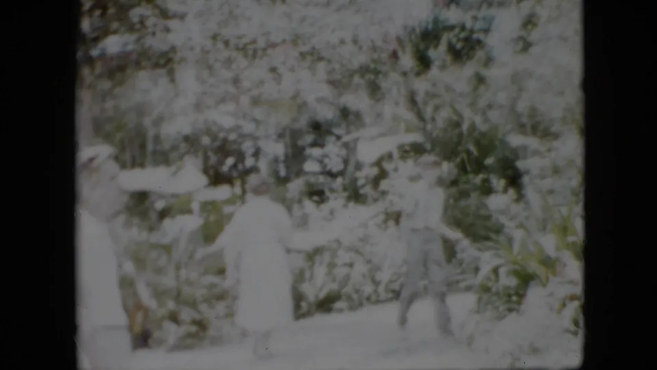 In this 1958 Pennsylvania home-movie frame, adults in light clothing appear amid dense greenery, with the scene strongly overexposed and softly focused.