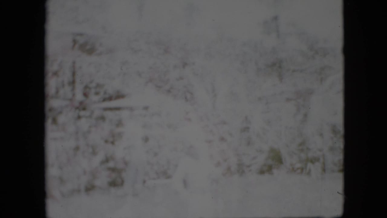 Faded 1958 Pennsylvania winter frame with snow-covered trees and barely visible structures or landscape forms in the background.