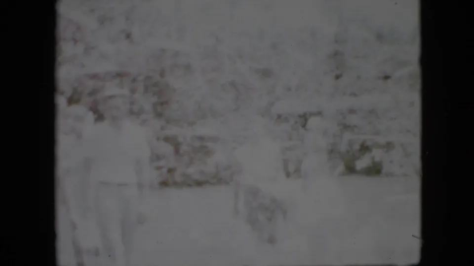 Faded 1958 Pennsylvania home-movie frame showing distant people in a bright outdoor garden or yard, with heavy grain and soft focus limiting identification.