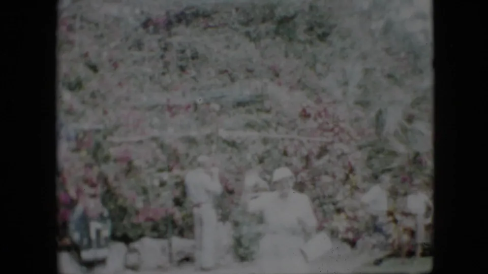 Faded 1958 Pennsylvania 8mm frame showing a light-clothed woman near several onlookers amid dense garden foliage.