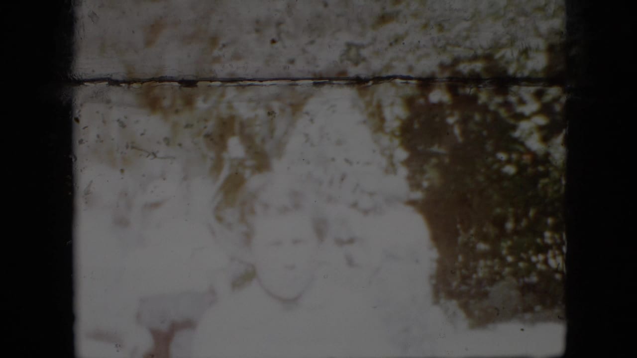 1958 Pennsylvania 8mm frame showing several adults in light clothing gathered outdoors near leafy trees, with faces softened by exposure and film wear.