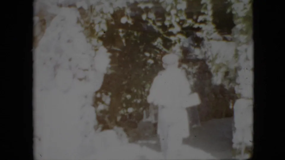 1958 Pennsylvania 8mm frame showing several adults in pale clothing gathered or walking in a shaded outdoor area with trees behind them.