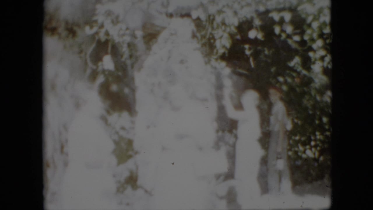 1958 Pennsylvania home-movie frame showing several people gathered in a wooded setting near a large pale statue, with strong overexposure obscuring facial detail.