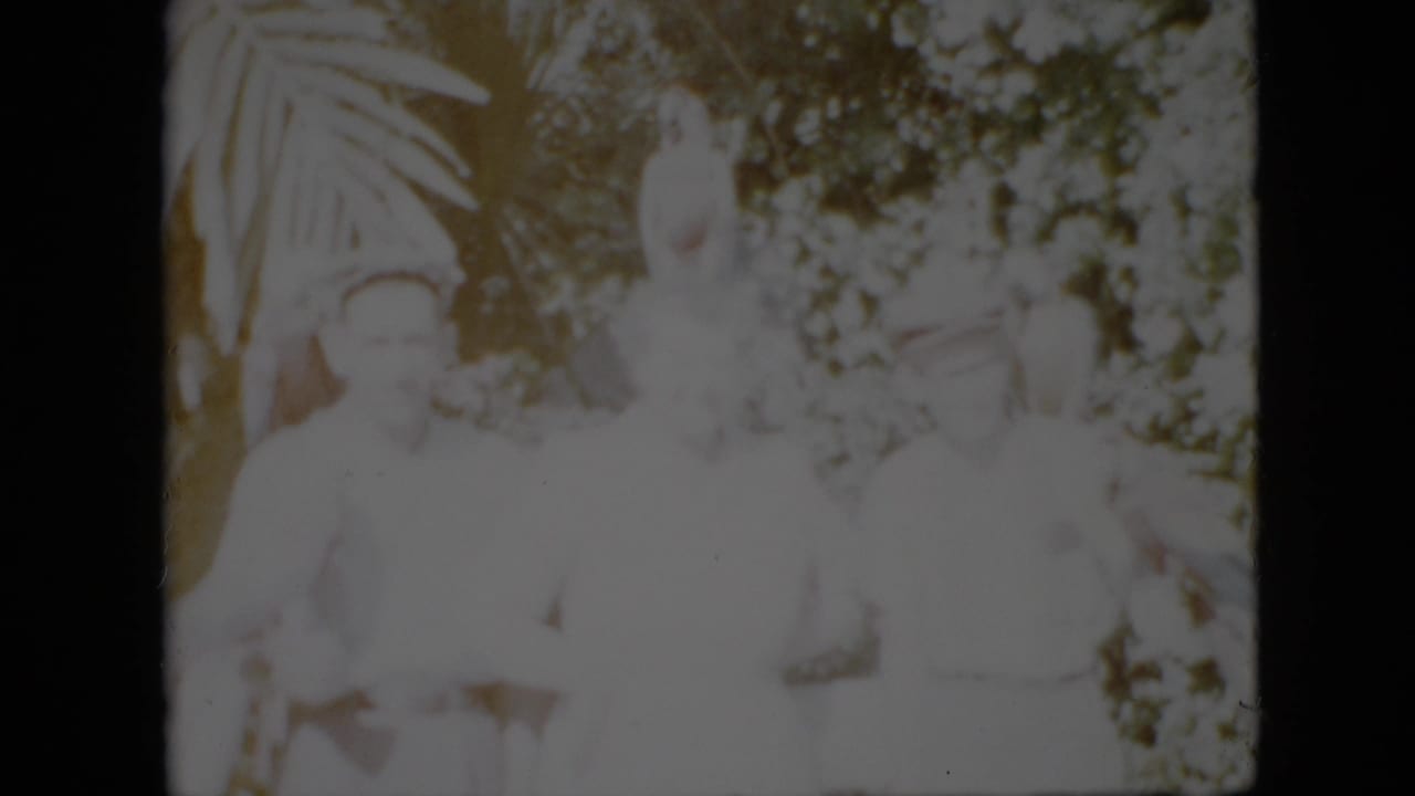 Two or more people in light clothing near a pale statue and dense foliage.