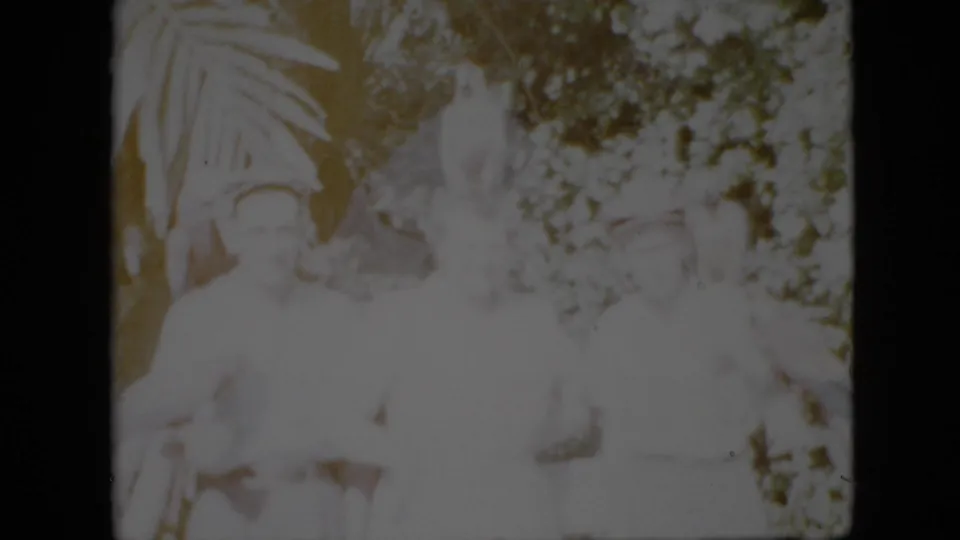 1958 Pennsylvania frame showing adults gathered in a wooded outdoor area beside a pale statue or sculpture, with soft focus and overexposed home-movie highlights.