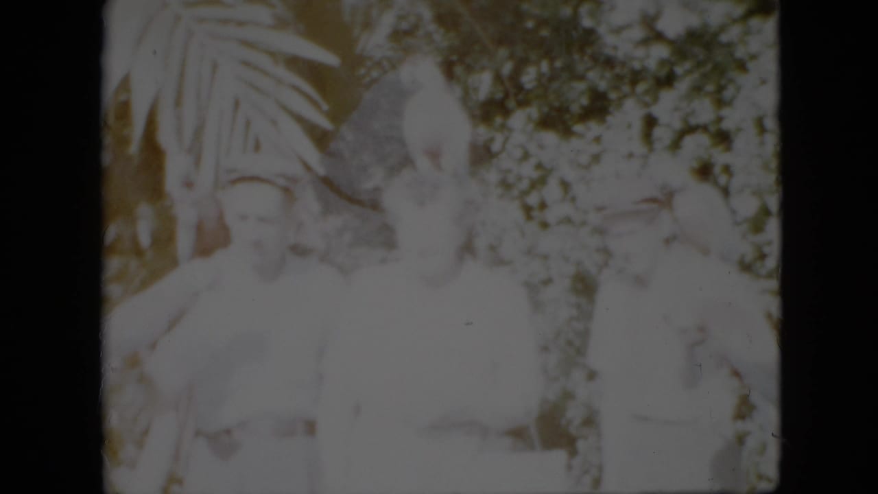 A small group stands among foliage with parrots visible near their shoulders and arms.