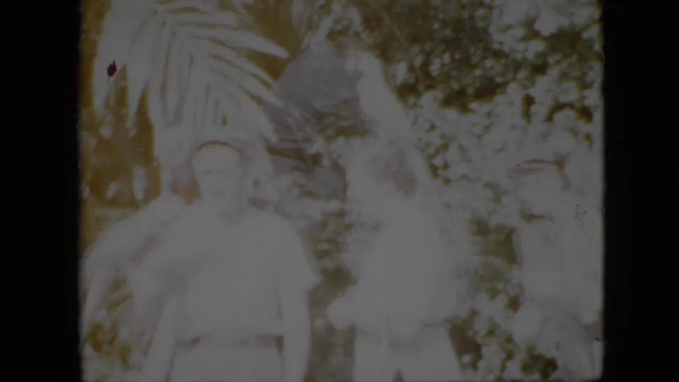 1958 Pennsylvania 8mm frame showing a man at left and other adults near parrots in a heavily exposed outdoor garden scene with broad leaves and bushes.